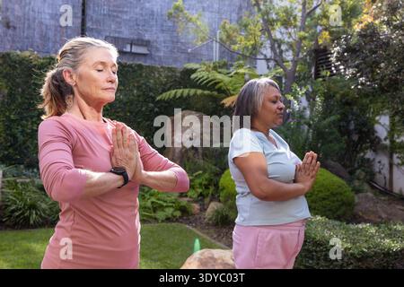 Verschiedene ältere Freundinnen meditieren im Garten mit rosa Oberteil und blauem Hemd mit schwarzer Uhr. Wellness, Entspannung, Achtsamkeit, Outdoor, Ruhe, Natur, Gesellschaft || Model veröffentlicht Stockfoto