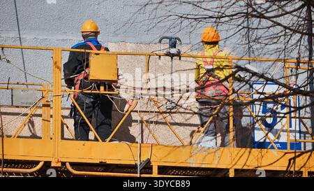 Lida, Weißrussland - 15. April 2025: Bauarbeiter renovieren die Gebäudefassade mit einer Hängeplattform Stockfoto