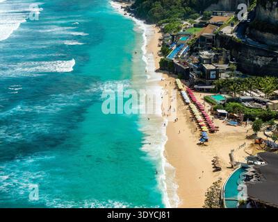 Türkisfarbene Meereswellen stürzen auf einen tropischen Sandstrand, der von farbenfrohen Sonnenschirmen gesäumt ist Stockfoto