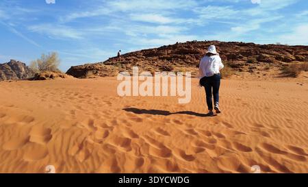 Eine weibliche Touristin, die entlang der orangefarbenen Sanddüne der berühmten geheimnisvollen Wüste Wadi Rum in Jordanien wandert Stockfoto