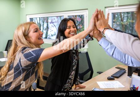 Glückliches, vielseitiges Büroteam, das Erfolge und Teamarbeit im Büro feiert Stockfoto