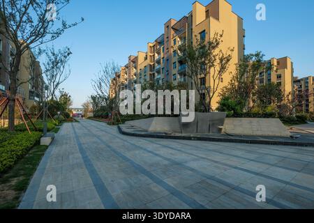 Blick auf die Landschaft eines sauberen, modernen Wohnapartments plaza mit gepflasterten Flächen, gepflegten Bäumen und Hochhäusern im Hintergrund. Stockfoto