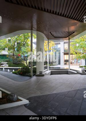 Ein zeitgenössischer, halb-außen-architektonischer Raum mit klaren Linien und Blick in einen üppig grünen Innenhof. Das Bild vermittelt modernen Luxus, Frieden Stockfoto