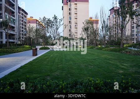 Ein ruhiger, landschaftlich gestalteter Wohnpark mit einem lebhaften grünen Rasen und modernen Apartmentgebäuden während des Abendübergangs. Das Bild übertragen Stockfoto