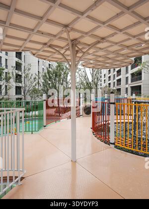 Ein lebendiger Kinderspielplatz mit modernem, schattigem Baldachin und farbenfrohen Sicherheitszäunen in einer Wohngegend. Das Bild vermittelt Verspieltheit, s Stockfoto