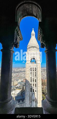 Blick auf den Glockenturm der Basilika Sacré-Cœur in Paris, eingerahmt von historischen Bögen und Säulen. Stockfoto