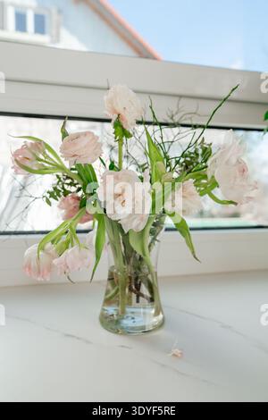 Blumenstrauß in einer durchsichtigen Vase am Fenster. Minimales Wohndesign und ruhiges Lifestyle-Konzept. Stockfoto