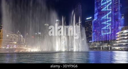 Abendliches Theater am Golf. Springbrunnen erheben sich aus der Lagune, während beleuchtete Türme die Szene in der Innenstadt von Dubai umrahmen. Berühmte Wassershow, die Globa anlockt Stockfoto