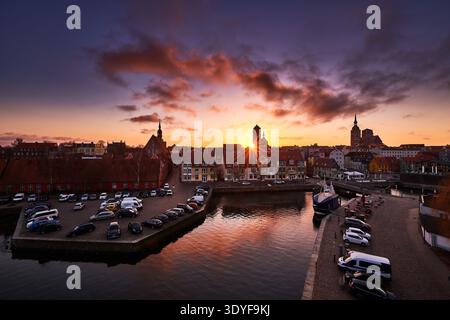 Erhöhter Panoramablick auf eine pulsierende europäische Küstenstadt bei einem atemberaubenden Sonnenuntergang. Der Sonnenschein blickt durch historische Gebäude und Kirchtürme, Stockfoto