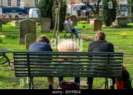 Drei junge Männer sitzen zusammen und entspannen sich in der Frühjahrssaison auf einer Bank auf einem Friedhof im Stadtzentrum von Oxford. Stockfoto