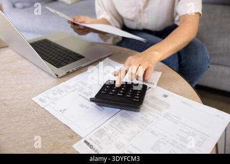 Eine junge Frau, die Papierrechnungen auf dem Rechner prüft, die Ausgaben zählt Stockfoto