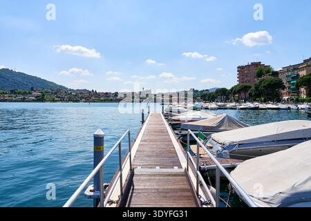 Ein malerischer Blick auf den Yachthafen in Sarnico, Italien, am Ufer des Iseosees. Hölzerne Piers erstrecken sich in ruhiges blaues Wasser, gesäumt von verankerten Yachten und Mot Stockfoto