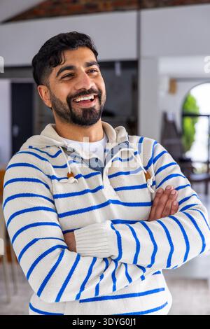 Erwachsener Mann lächelt in einem hellen, offenen Haus mit Strickpullover mit Knebel, Torbogen-Topfpflanze Stockfoto