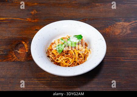 Eine Schüssel Spaghetti sitzt auf einem Holztisch. Auf dem Gericht stehen Kräuter und Käse. Die Umgebung ist einfach und konzentriert sich auf das Essen. Stockfoto