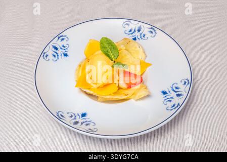 Dieses Bild fängt die lebendige Palette des Sommers mit würfeln süßer, reifer Mango ein, begleitet von roten Beeren, Kiwis und Minzblättern, die alle mit getoppt werden Stockfoto