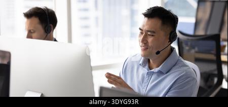Junger Mann Hotline-Betreiber im Headset Kontakt mit dem Kunden über den Computer Stockfoto