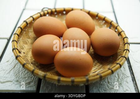 Braune Hühnereier in einem traditionellen Bambuskorb auf einem Küchentisch. Frische rohe Eier als natürliche Lebensmittelzutat, die häufig beim Kochen verwendet wird Stockfoto
