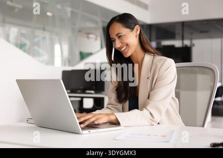 Positive Geschäftsfrau sitzt am Schreibtisch und arbeitet am Laptop Stockfoto