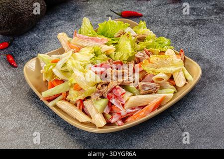 Appetitlicher Nudelsalat mit Thunfisch und Gemüse in einer cremigen Sauce. Die Top-Down-Ansicht auf dunklem Hintergrund hebt frische rote, grüne und beige Farben hervor. P Stockfoto