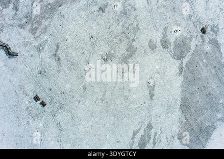 Gefrorene, schneebedeckte Landschaft mit Militärgräben und runden Fahrzeugwegen unter kaltem Winterlicht. Dieser strukturierte abstrakte Hintergrund zeigt eine raue und öde saisonale Umgebung. Stockfoto