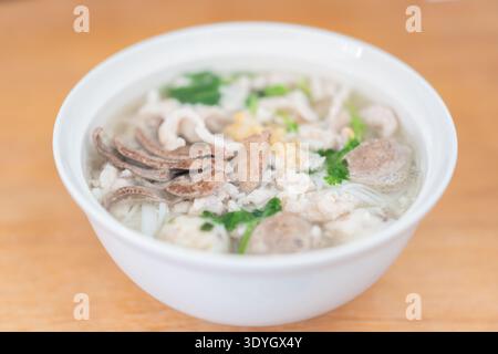 Vietnamesische Pho-Nudelsuppe mit Rinderkraut und Kräutern in der weißen Schüssel auf Holztisch Stockfoto