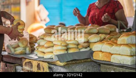 Brot und Gebäck an einem Marktstand im Freien. Verkauf von frisch gebackenem, hausgemachtem Brot und Essen auf der Straße. Traditionelles Goa-Brot. Frau, die Einheimische kauft Stockfoto