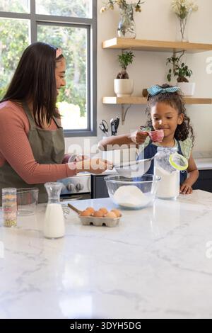 Afroamerikanische Mutter und Kind tragen Schürze und Schürze, die Mehl auf Marmortheke sickern Stockfoto