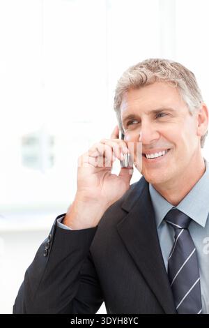 Senior Mann im dunklen Anzug, gestreifte Krawatte hält Smartphone am Ohr im Büro, lächelt, Kopierraum. Executive, Corporate, Professional, Telefon, Hintergrundbeleuchtung, HG Stockfoto