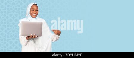 Frau hält Laptop und lächelt, während sie auf den Bildschirm zeigt Stockfoto