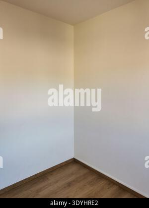 Innenaufnahme zeigt tagsüber die Ecke eines leeren Raumes an. Die Wände sind in weiß und Beige gestrichen und verfügen über einen Holzfußboden Stockfoto