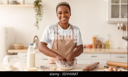 Frau, die Teig in der Küche zubereitet, während sie lächelt und die Schüssel mit Zutaten mischt Stockfoto