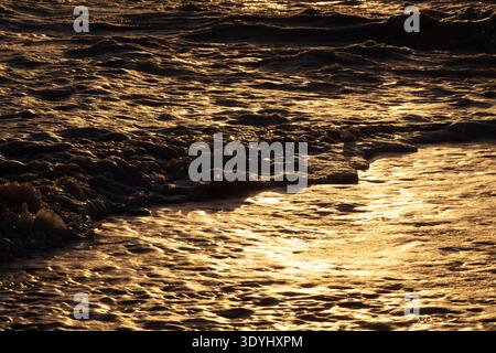 Ozeanwellen brechen bei Sonnenuntergang am Ufer, Licht reflektiert vom Wasser. Stockfoto