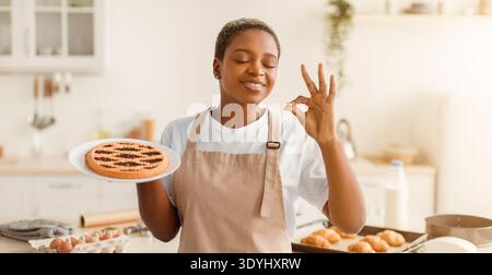 Eine Frau steht in einer hellen Küche und hält einen Teller mit Keksen Stockfoto