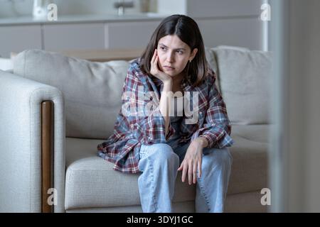 Gelangweilt frustrierte junge Frau sitzt zu Hause auf dem Sofa Gesicht an Hand mit entferntem Blick fühlt inneren Konflikt Stockfoto