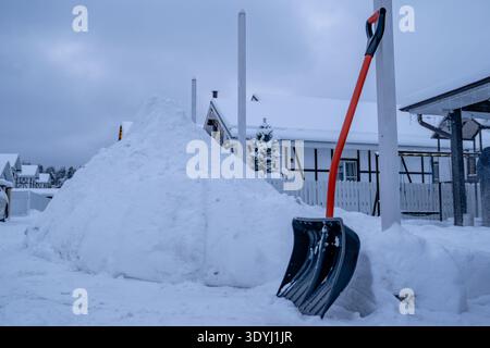 Schneeschaufel steht auf hohem Schneehaufen in der Nähe der Vorstadteinfahrt. Manuelle Schneeräumung nach Schneefall Stockfoto