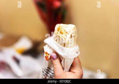 Nahaufnahme einer Hand, die eine frisch gegrillte Hähnchenhawarma-Wrap hält. Stockfoto