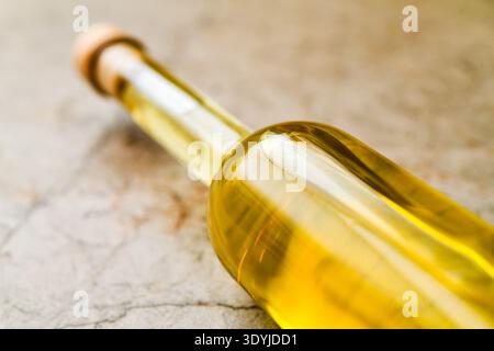 Nahaufnahme einer Klarglasflasche gefüllt mit gelbem selbstgemachten Quittenlikör auf einer texturierten Steinoberfläche mit Korkstopfen. Stockfoto