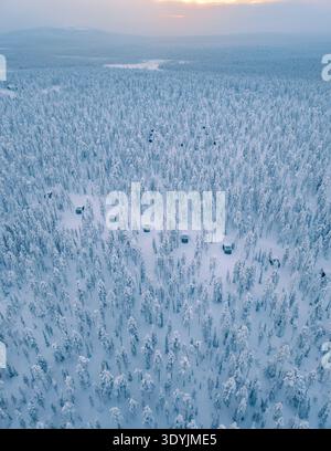 Erleben Sie die unberührte Schönheit von Akaslompolo in Lappland, Finnland, mit gemütlichen Hütten, eingebettet zwischen einer riesigen Fläche von schneebedeckten Bäumen bei einem weichen Wintersonnenuntergang. Stockfoto