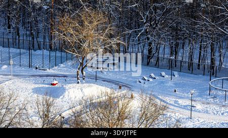 Panoramablick auf den sonnigen, schneebedeckten Spielplatz in der Nähe des Stadtparks an sonnigen Wintertagen Stockfoto