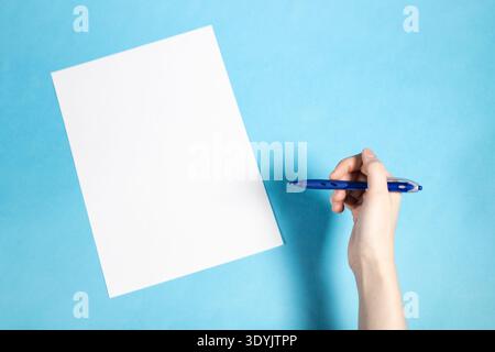 Draufsicht des leeren weißen Papiers und der Hand hält den Stift auf blauem Papierhintergrund Stockfoto