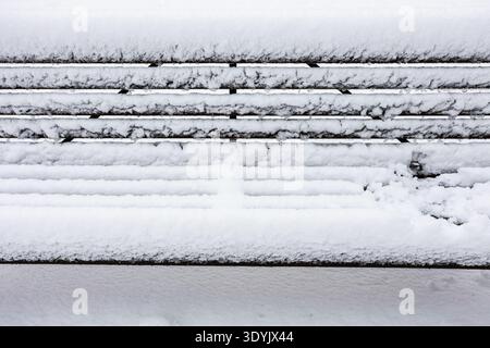 Schneebedeckter Sitz einer Holzbank im Stadtgarten nach Schneefall an bewölktem Wintertag Stockfoto