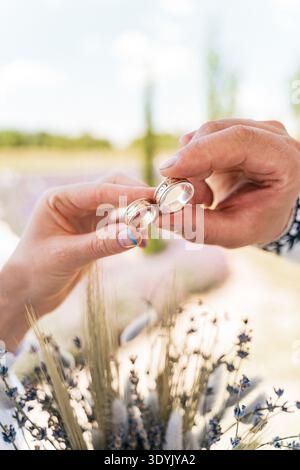 Ein Paar hält Eheringe über einem getrockneten Blumenstrauß. Hochzeitszeremonie im rustikalen Stil Stockfoto