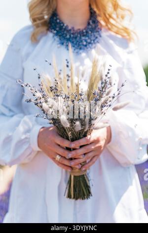 Frau in weißem Kleid hält einen getrockneten Lavendelstrauß. Sommermode, rustikaler Stil Stockfoto