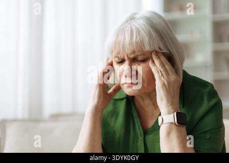 Ältere Frau berührt Schläfe, während sie zu Hause Kopfschmerzen hat Stockfoto