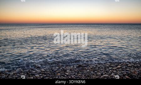 Sanfte Wellen am Kiesstrand und ruhiges Mittelmeer bei Sonnenuntergang in Kato Zakros, Kreta, Griechenland. Minimale Küstenszene mit sanften Abendfarben und pe Stockfoto