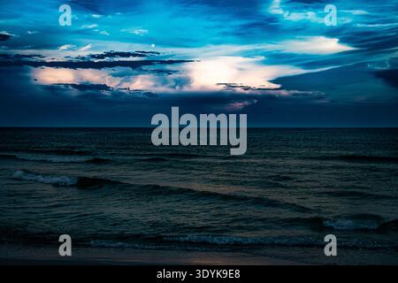 Blauer Horizont. Das Abendlicht breitet sich über einen ruhigen Ozean aus, während die geschichteten Gewitterwolken über dem fernen Horizont leuchten. Stockfoto