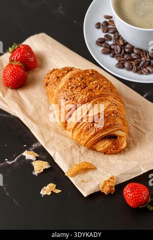 Frisch gebackene Butter Nougat zerstoßene Nüsse Frühstückscroissant, Kaffeetasse mit Bohnen und Krümeln auf dunklem Marmortisch Stockfoto