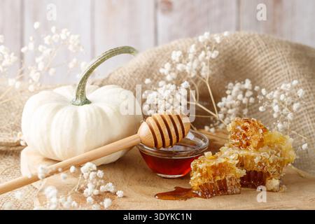 Goldene Waben mit frischem natürlichem Honig und Glasschale mit Pendelarm mit weißem Kürbis und Blumen. Frische Ernte von dunklem Waldhonig Stockfoto