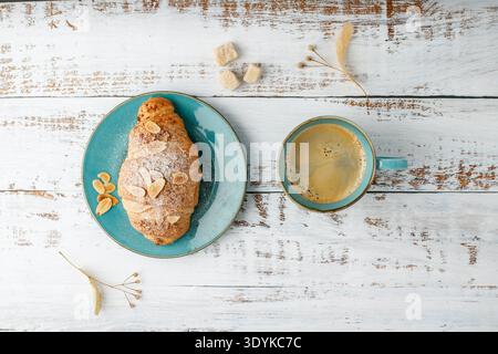 Frisch gebackene Mandelnüsse Frühstück Croissant auf Vintage türkisfarbenen Teller und heiße Kaffeetasse auf rustikalem hölzernem Hintergrund. Gebäck mit Blick von oben Guten Morgen, ca. Stockfoto