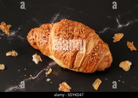 Frisch gebackene Butter, Mandelnüsse, Croissant und Krümel auf dunklem Marmortisch. Ein Croissant in der Nähe. Stockfoto